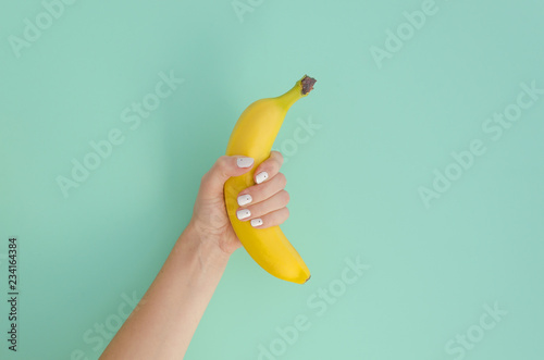 Fotografie, Tablou Female hand holding a banana on a mint background