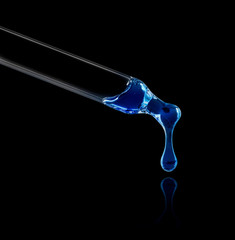 Wall Mural - Blue liquid drop from cosmetic pipette close up on black background