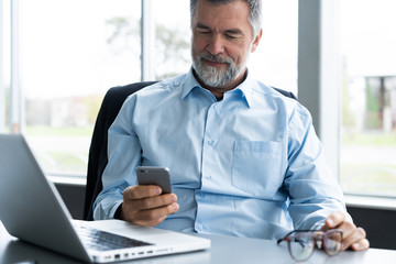 Mature business man in formal clothing using mobile phone. Serious businessman using smartphone at work. Manager in suit using cellphone in a modern office.