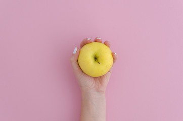 a yellow apple in a lady's hand on pink background