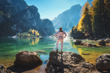 Wall Mural - standing sporty man on the stone on the coast of braies lake at sunrise. autumn in dolomites, italy.