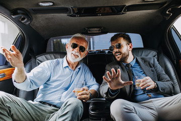 Wall Mural - Senior businessman and his assistant sitting in limousine and celebrating their job success.