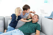 Little Children Painting Their Father's Face While He Sleeping On Couch At Home. April Fool's Day Prank
