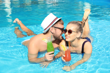 Canvas Print - Young couple with refreshing cocktails in swimming pool at resort