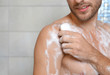 © New Africa - Young man taking shower with soap in bathroom, closeup. Space for text