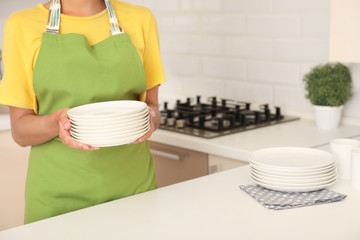 Poster - Woman holding stack of clean dishes in kitchen