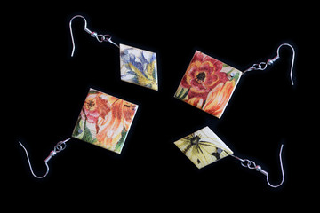 Two pairs of wooden earrings with a floral print on a dark background close up