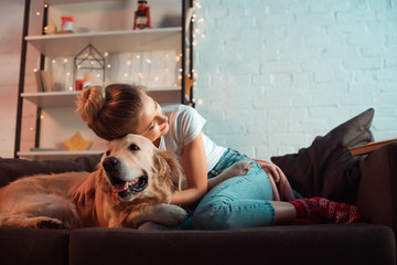 young blonde woman on couch hugging golden retriever dog at christmas time