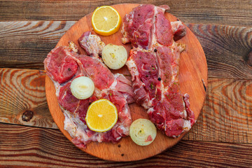 Fresh raw pork meat with spices, lemon and onion on wooden cutting board on rustic table. Top view