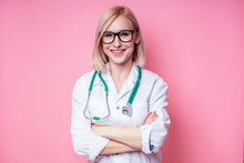 Portrait Of A Smiling Female Gynecologist Doctor.beautiful Blonde Woman In White Medical Coat And Glasses Holding A Stethoscope On A Pink Background In The Studio.beautician Perfect Skin