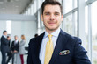 © opolja - Young and confident businessman. Handsome young man in formalwear smiling at camera while his colleagues working on background.
