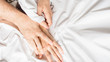 © Stavros - couples hold hands together in bed close-up touching each other on a white blanket.