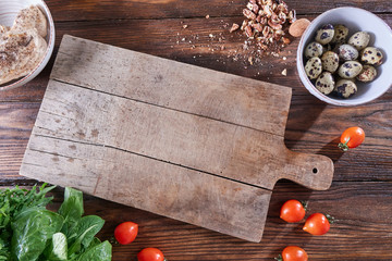 wooden board on the kitchen table around boiled quail eggs in a bowl, pieces of nuts, tomatoes, meat
