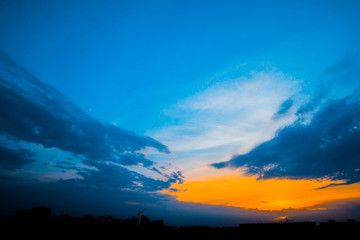Wall Mural - atmospheric blue cloudy sky behind silhouettes of city buildings. purple and orange background of su