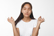 © shurkin_son - Meditation, concentration, harmony and balance concept. Studio image of brunette Chinese girl closing eyes and holding hands in mudra gesture, having calm peaceful restful look while meditating