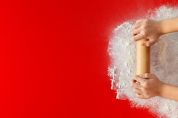 Young hands with rolling pin and flour on red table - large copy space