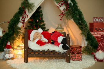 Canvas Print - Adorable little toddler baby boy dressed in canta claus costume, sleeping in baby bed in front of crhistmas teepee