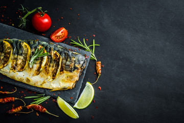 Wall Mural - Grilled fish fillets with lime on black slate board, mackerel with vegetables and herbs