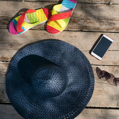 Blue straw hat, sunglasses, beach slippers and phone on old wooden boards.