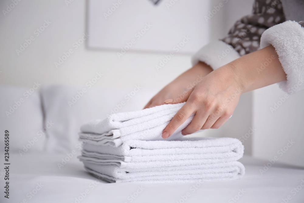 Woman putting clean white towels on bed indoors