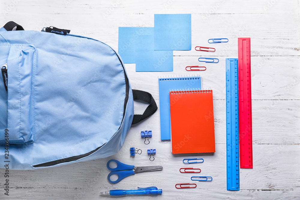 Composition with rucksack and school stationery on light background, top view