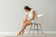 © Pixel-Shot - Woman suffering from pain in leg while sitting on chair near light wall