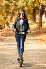 Sticker - Beautiful young woman riding on scooter in autumn park