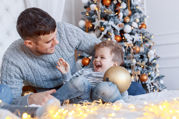 Wall Mural - A daddy with his two sons twins in front of the christmas tree  with candles and gifts hugging and having fun. New year's eve. Cozy holiday at the fir-tree. love, happiness and big family concept