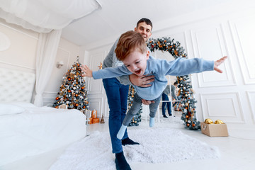 Wall Mural - A daddy with his two sons twins in front of the christmas tree  with candles and gifts hugging and having fun. New year's eve. Cozy holiday at the fir-tree. love, happiness and big family concept