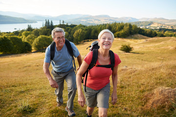 portrait of senior couple climbing hill on hike through countryside in lake district uk together