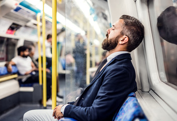 Wall Mural - Sleeping hipster businessman inside the subway in the city, travelling to work.