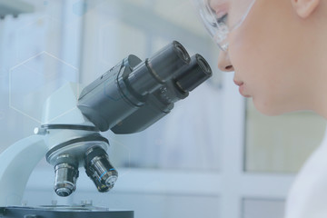 Wall Mural - Young female scientist looking through a microscope in a laboratory doing research, microbiological analysis, medicine.