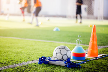 Wall Mural - Football and soccer training equipment on green artificial turf with blurry players training background.