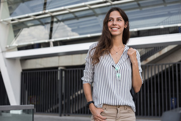 Portrait of attractive young hipster girl, trendy outfit and glasses strolling in morning of spring sunny day while waiting for friend, charming female traveler having positive mood near offise center