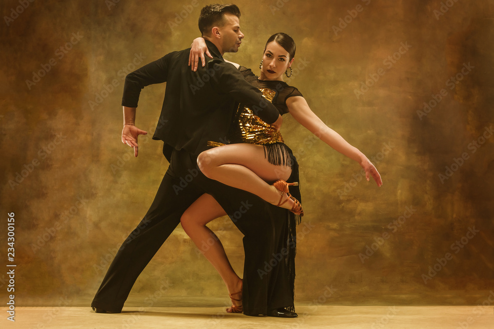 The young dance ballroom couple in gold dress dancing in sensual pose on studio background. Professional dancers dancing tango. Ballroom dance concept. Human emotions - love and passion - obrazy, fototapety, plakaty 