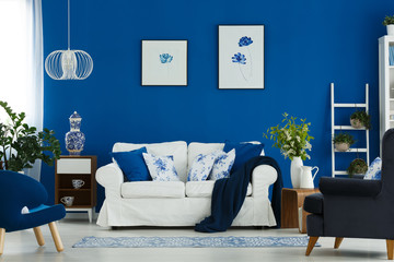 Floral poster on blue wall in chic living room interior with white, blue and wooden furniture in contemporary living room