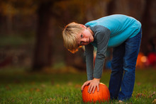 Boy In A Garden Bending Over To Pick Up A Pumpkin, United States
