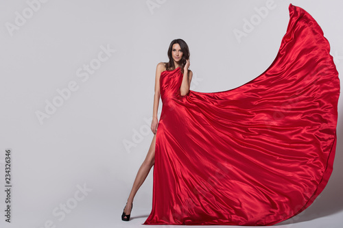 Foto Beauty young woman in fluttering red dress. Gray background.