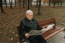 Elderly Man Reading Newspaper In Park