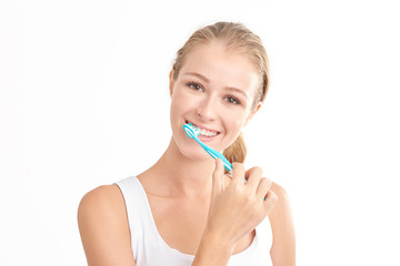 Beautiful young woman brushing her teeth against white background