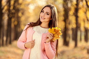 Beautiful woman with maple leafs in autumn park