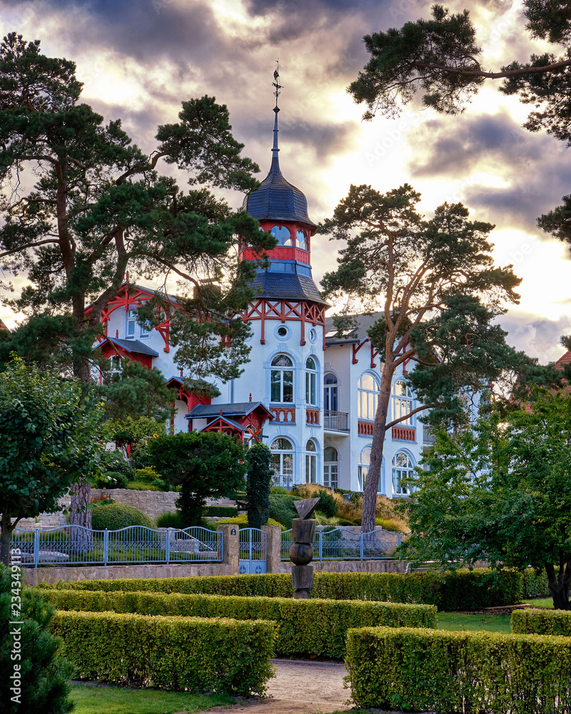 Park with old Baltic house with trees in the sunshine on the beach promenade Zinnowitz on the island of Usedom. - obrazy, fototapety, plakaty 