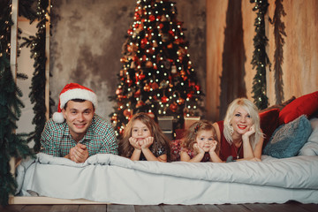 Merry Christmas and Happy Holidays! Cheerful parents and and two little children having fun and playing together near Christmas tree on the bed in living room