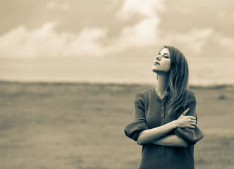 Wall Mural - Beautiful adult girl in sweater at wheat field and cloudscape on background. Image in sepia color style