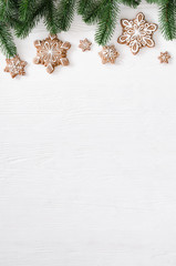 Christmas homemade gingerbread cookies and fir branches on white wooden background.