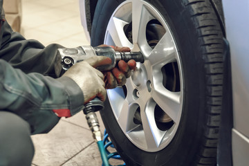 Replacing summer tires for winter using pneumatic wrench tool by mechanic worker after balancing wheels in car service garage shop