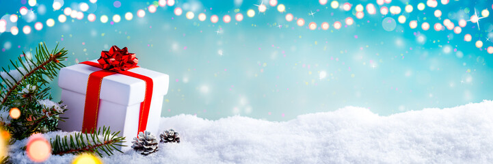 christmas gift box, fir branches and pine cones, on snow with christmas lights