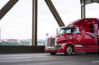 Red modern big rig semi truck driving on the bridge transporting commercial cargo in refrigerated semi trailer
