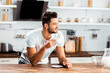 smiling young man holding cup of coffee and leaning at kitchen table at morning