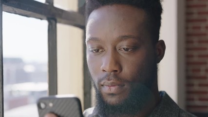 portrait young african american man using smartphone at home browsing messages networking texting social media sharing lifestyle online planning ahead in modern apartment close up